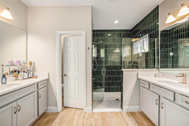 full bathroom featuring a stall shower, two vanities, a sink, and wood finished floors