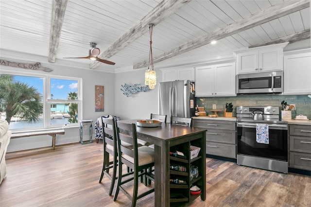 kitchen featuring stainless steel appliances, light countertops, decorative backsplash, light wood-style floors, and beamed ceiling