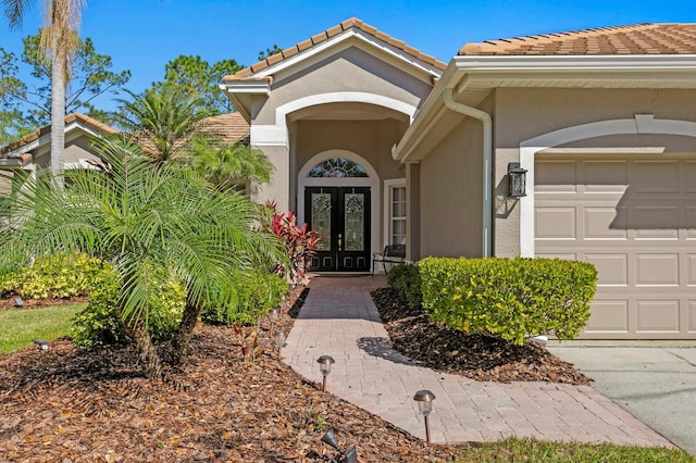 entrance to property featuring french doors, a tiled roof, an attached garage, and stucco siding