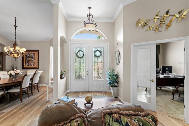 foyer with arched walkways, french doors, an inviting chandelier, light wood-style floors, and ornamental molding