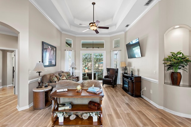 living area with arched walkways, light wood-style flooring, a ceiling fan, baseboards, and a tray ceiling