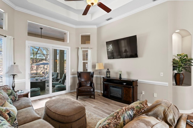 living room with ceiling fan, wood finished floors, visible vents, a tray ceiling, and a glass covered fireplace