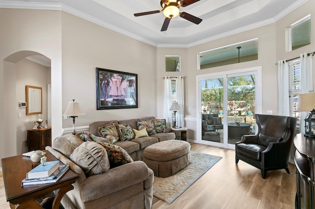 living area with light wood-type flooring, arched walkways, a tray ceiling, and ornamental molding