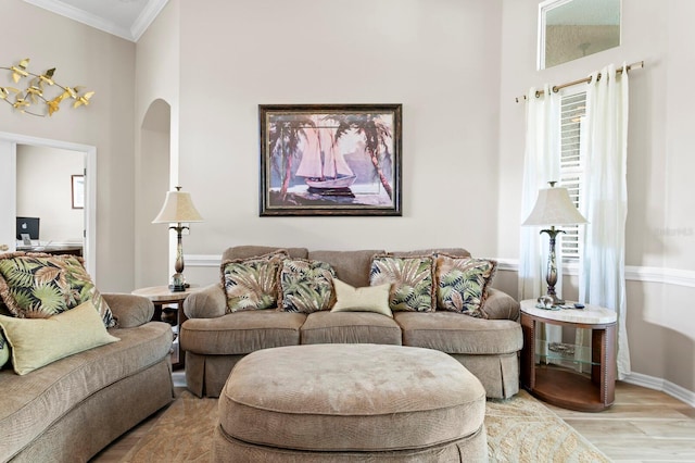 living area with arched walkways, light wood-style floors, baseboards, and crown molding