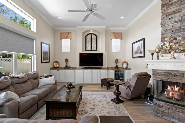 living area featuring ornamental molding, a fireplace, light wood-style flooring, and a ceiling fan