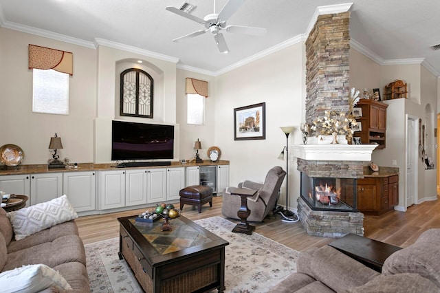 living area with crown molding, a stone fireplace, and light wood finished floors