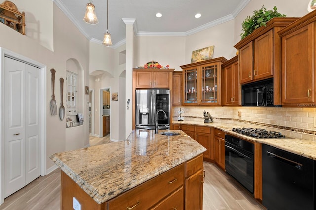 kitchen with light wood-style flooring, brown cabinets, light stone countertops, black appliances, and backsplash