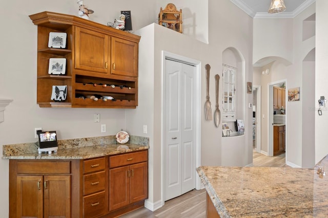 bar with arched walkways, a high ceiling, ornamental molding, light wood-type flooring, and baseboards