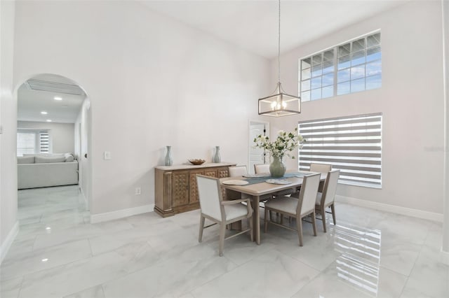 dining area featuring arched walkways, marble finish floor, a high ceiling, an inviting chandelier, and baseboards