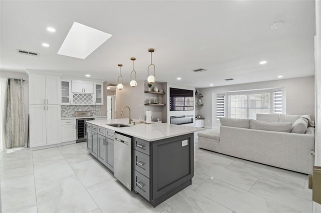 kitchen featuring white cabinets, dishwasher, glass insert cabinets, open floor plan, and a sink