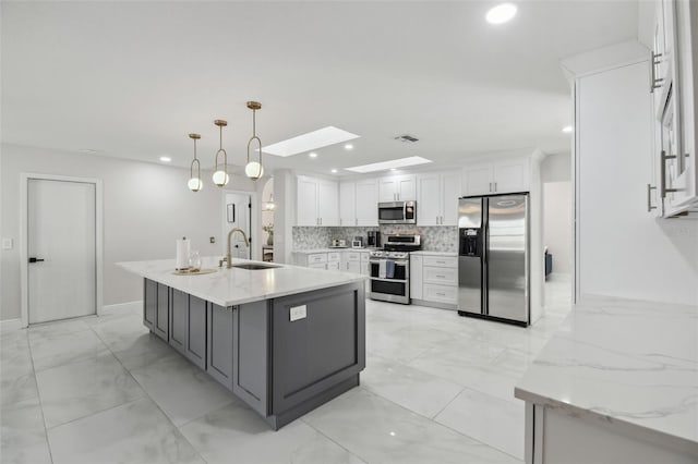 kitchen featuring light stone counters, hanging light fixtures, appliances with stainless steel finishes, white cabinetry, and a sink