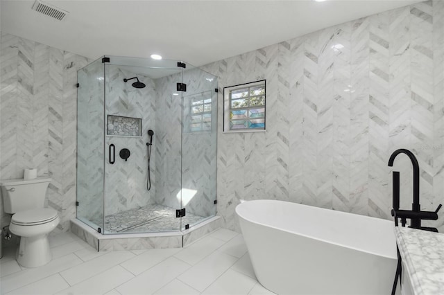 full bath featuring toilet, vanity, visible vents, a freestanding bath, and tile walls