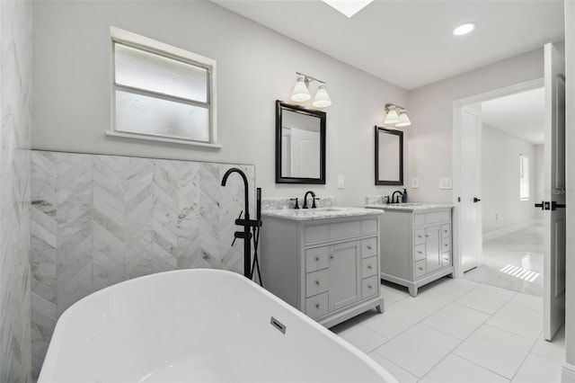 full bath featuring a soaking tub, two vanities, tile patterned floors, a sink, and tile walls