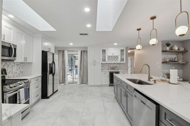 kitchen with white cabinets, glass insert cabinets, decorative light fixtures, stainless steel appliances, and a sink