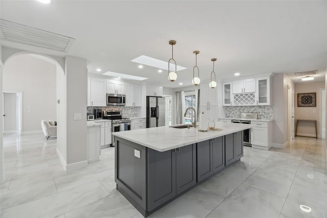 kitchen featuring a center island with sink, stainless steel appliances, glass insert cabinets, white cabinets, and a sink