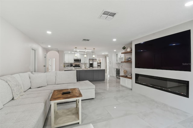 living room with beverage cooler, visible vents, arched walkways, a glass covered fireplace, and marble finish floor