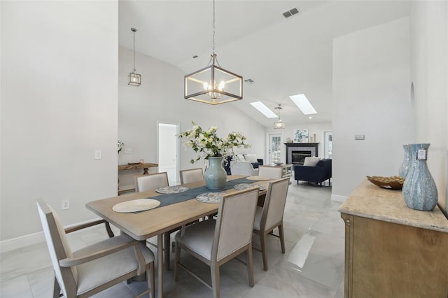 dining room featuring marble finish floor, visible vents, vaulted ceiling with skylight, baseboards, and a tile fireplace