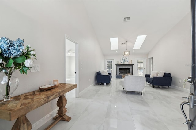 living area featuring a skylight, baseboards, visible vents, a glass covered fireplace, and high vaulted ceiling