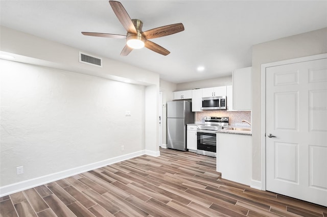 kitchen featuring wood finish floors, stainless steel appliances, visible vents, backsplash, and white cabinets