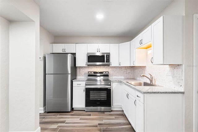 kitchen with appliances with stainless steel finishes, white cabinets, a sink, and decorative backsplash