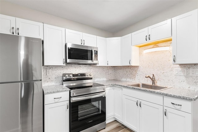 kitchen with backsplash, white cabinetry, stainless steel appliances, and a sink