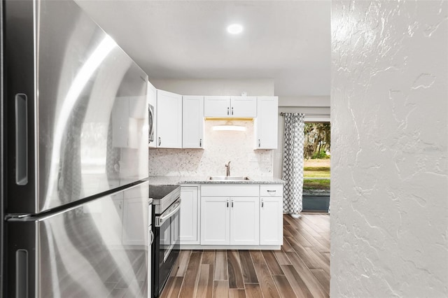 kitchen with decorative backsplash, a textured wall, dark wood-type flooring, stainless steel appliances, and a sink