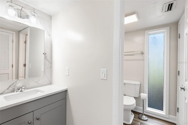 bathroom with toilet, wood finished floors, vanity, visible vents, and baseboards