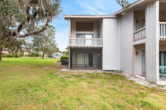 rear view of property featuring a lawn, cooling unit, and a balcony