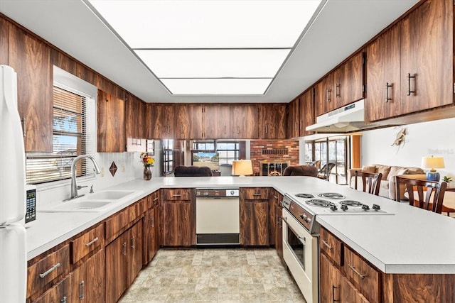 kitchen with light countertops, a sink, a peninsula, white appliances, and under cabinet range hood