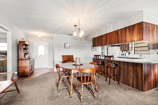 carpeted dining room featuring a healthy amount of sunlight, a textured ceiling, a chandelier, and a sink