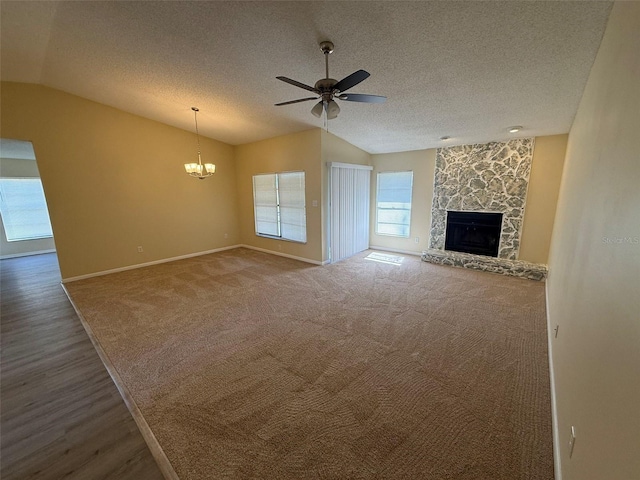 unfurnished living room featuring lofted ceiling, ceiling fan with notable chandelier, a textured ceiling, and a stone fireplace