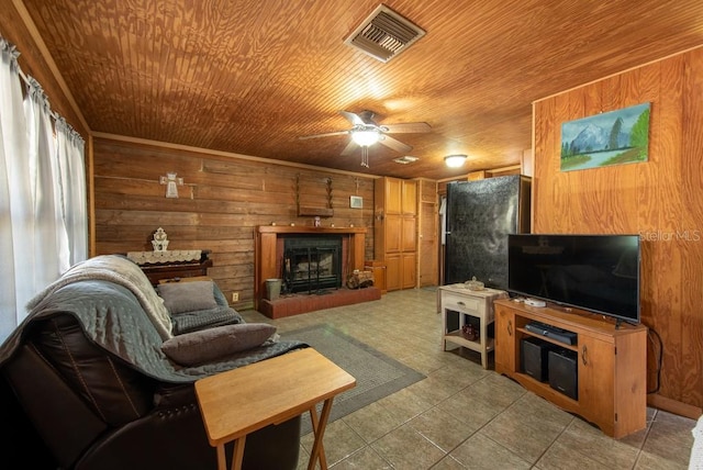 living room featuring light tile patterned floors, visible vents, a fireplace with raised hearth, wood walls, and wooden ceiling