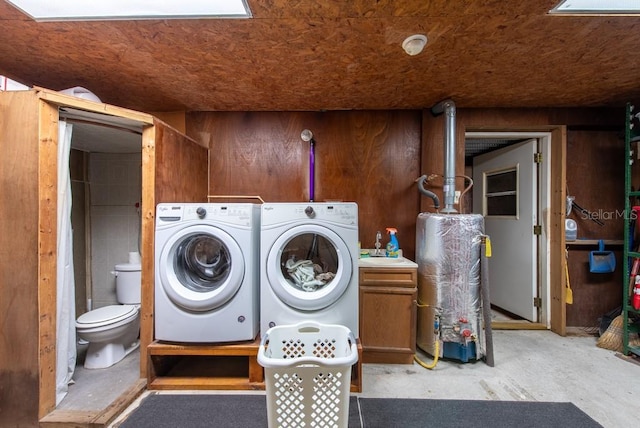 laundry room featuring laundry area, water heater, washer and clothes dryer, and wood walls