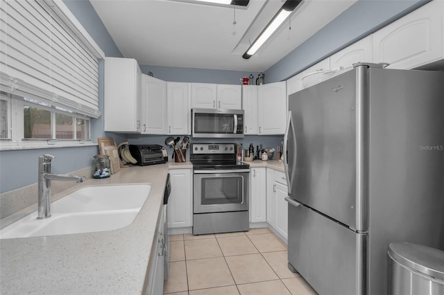 kitchen featuring light tile patterned floors, stainless steel appliances, light countertops, white cabinets, and a sink