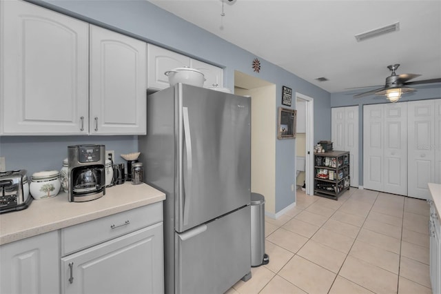 kitchen featuring light tile patterned floors, light countertops, visible vents, freestanding refrigerator, and white cabinetry