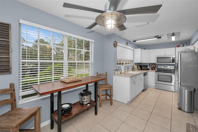 kitchen with white cabinets, stainless steel appliances, light countertops, a sink, and light tile patterned flooring