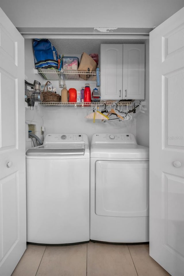 clothes washing area with separate washer and dryer, light tile patterned flooring, and cabinet space