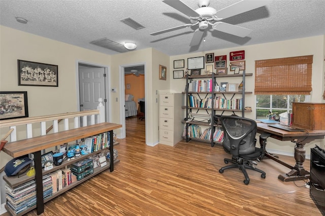 home office with light wood-type flooring, a ceiling fan, visible vents, and a textured ceiling