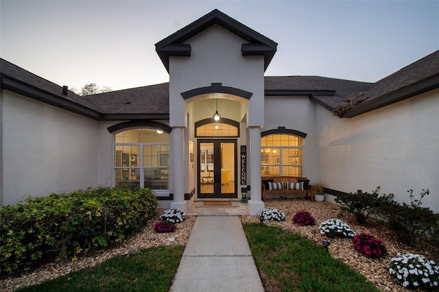 entrance to property featuring french doors, roof with shingles, and stucco siding