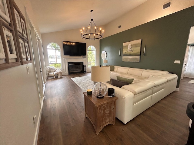 living area featuring visible vents, a glass covered fireplace, dark wood-style flooring, vaulted ceiling, and a notable chandelier