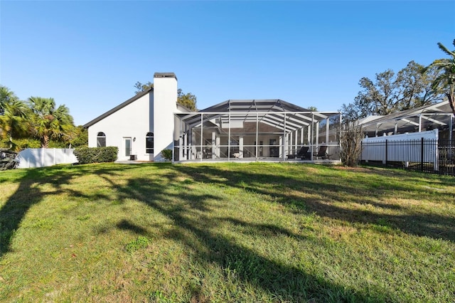 rear view of house with a chimney, fence, a lawn, and a lanai