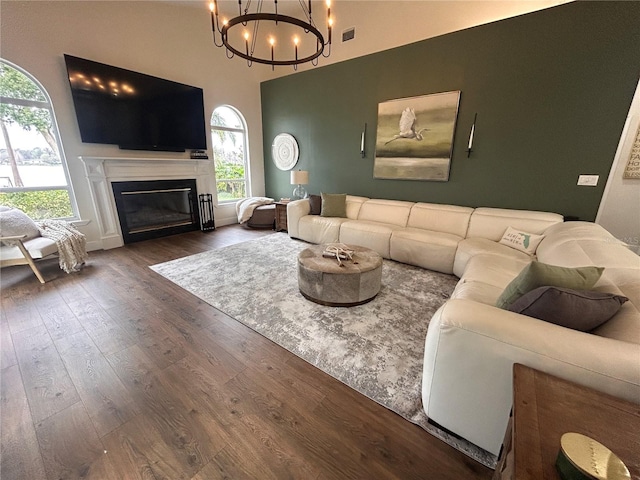 living area with dark wood-type flooring, a glass covered fireplace, visible vents, and a notable chandelier