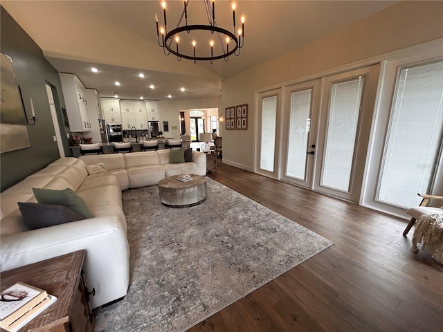 living area with dark wood-style flooring, lofted ceiling, recessed lighting, an inviting chandelier, and baseboards