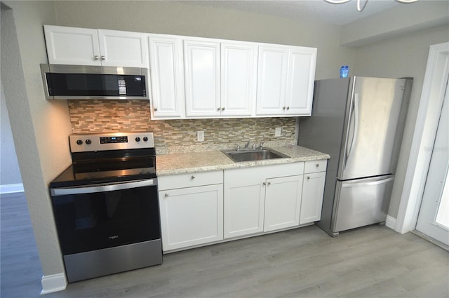 kitchen with a sink, white cabinets, light wood finished floors, appliances with stainless steel finishes, and tasteful backsplash