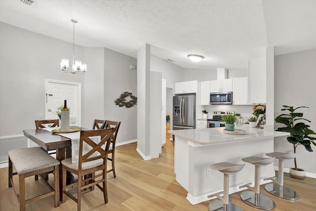 kitchen featuring stainless steel appliances, a peninsula, white cabinetry, light countertops, and decorative light fixtures