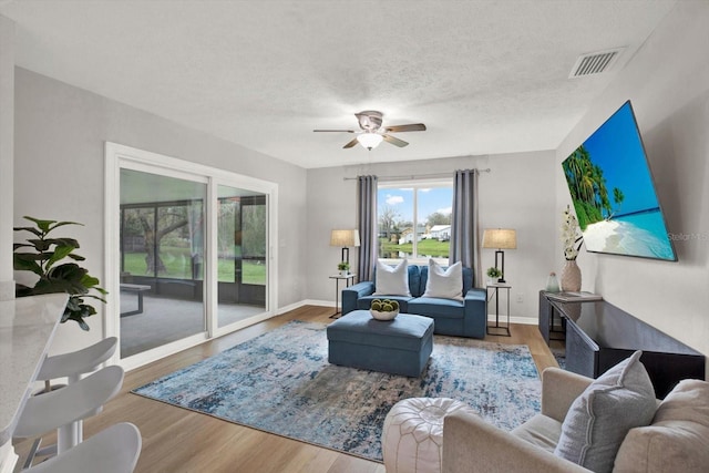 living room with a textured ceiling, ceiling fan, wood finished floors, visible vents, and baseboards