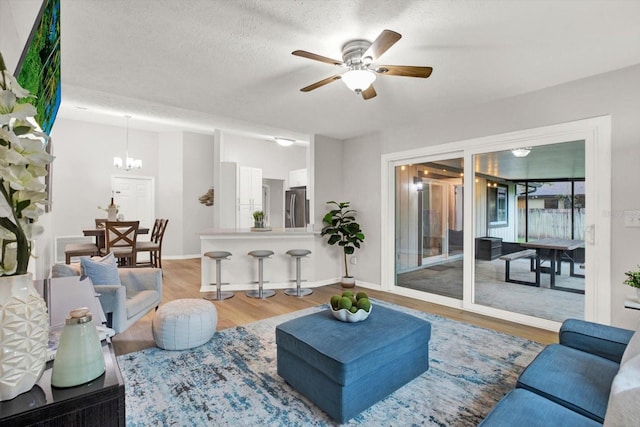 living room with a textured ceiling, ceiling fan with notable chandelier, wood finished floors, and baseboards