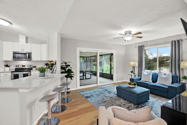 living area with ceiling fan, a textured ceiling, light wood-style flooring, baseboards, and vaulted ceiling