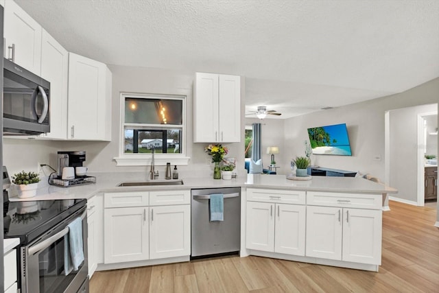 kitchen with stainless steel appliances, light countertops, white cabinetry, a sink, and a peninsula