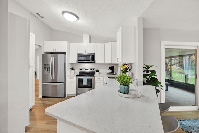 kitchen with light wood finished floors, visible vents, white cabinets, lofted ceiling, and stainless steel appliances